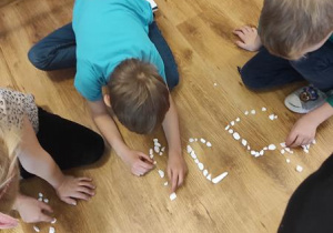 Dzieci układają z kamyczków kształt litery i.